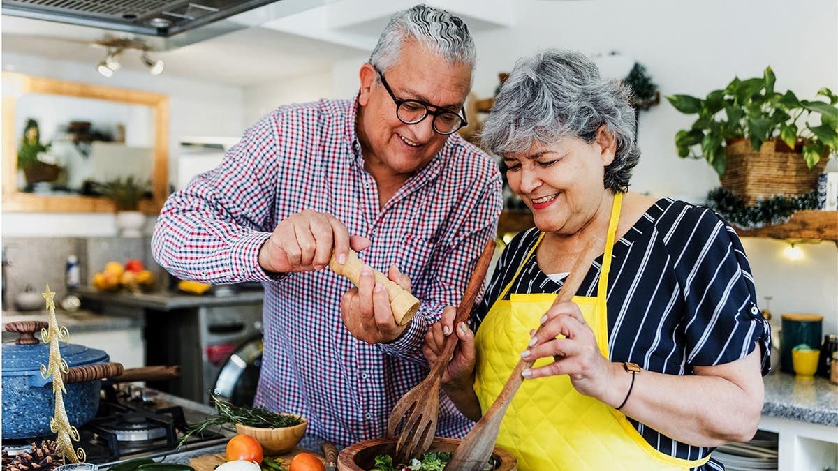 An older couple cooks in a kitchen together.