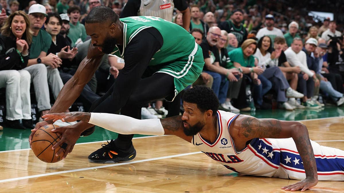 Philadelphia 76ers forward Paul George and Boston Celtics guard Jaylen Brown competing for a loose ball during a basketball game.