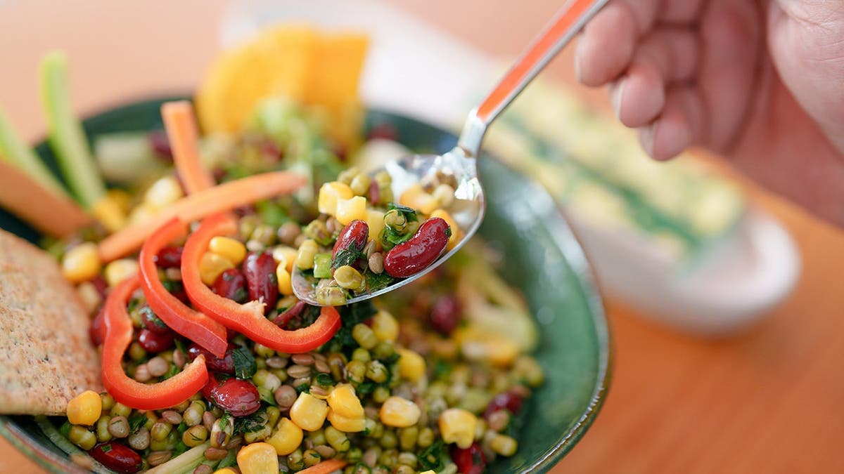 A person eats a bowl of vegetables with a fork.