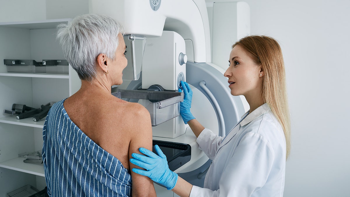 Senior woman undergoing mammography scan with medical technician at hospital