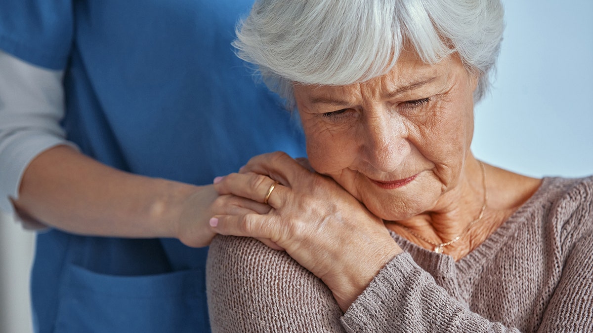Nurse consoling a senior woman seated in a nursing home room