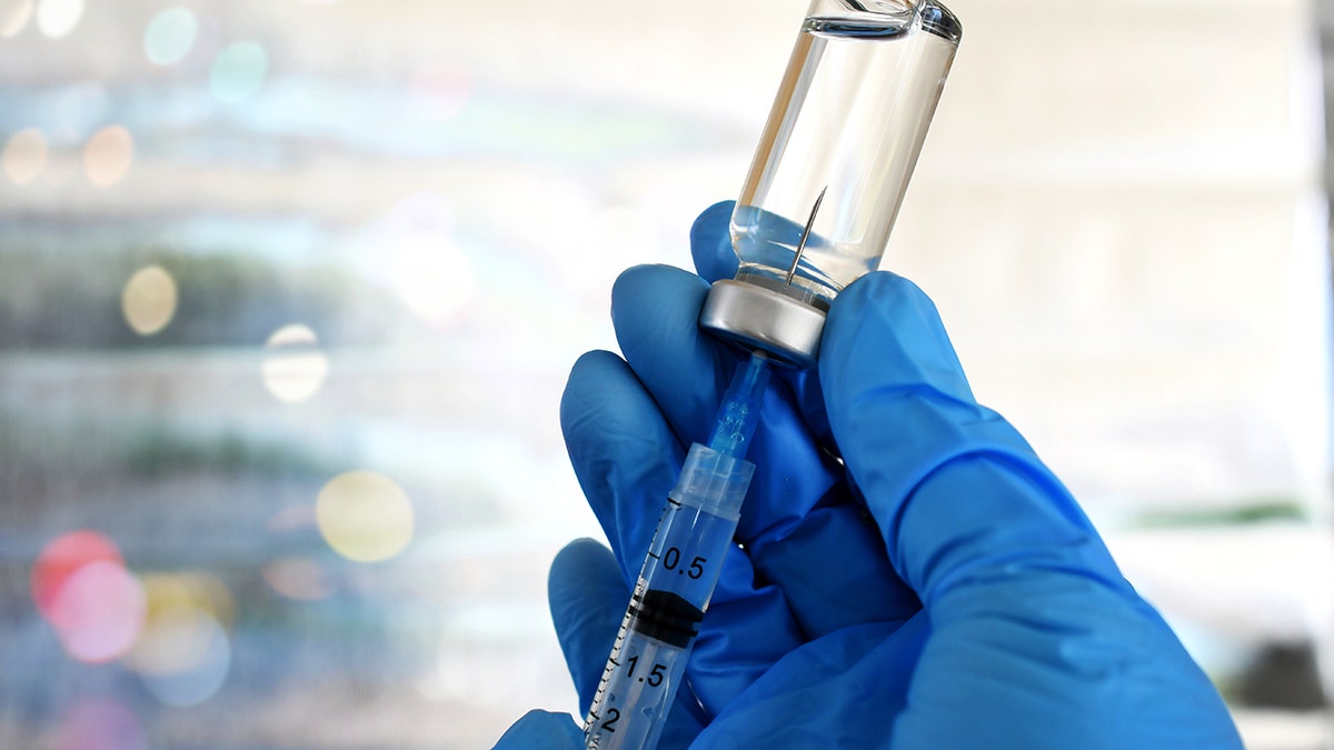 Hand holding syringe inserted in vaccine vial