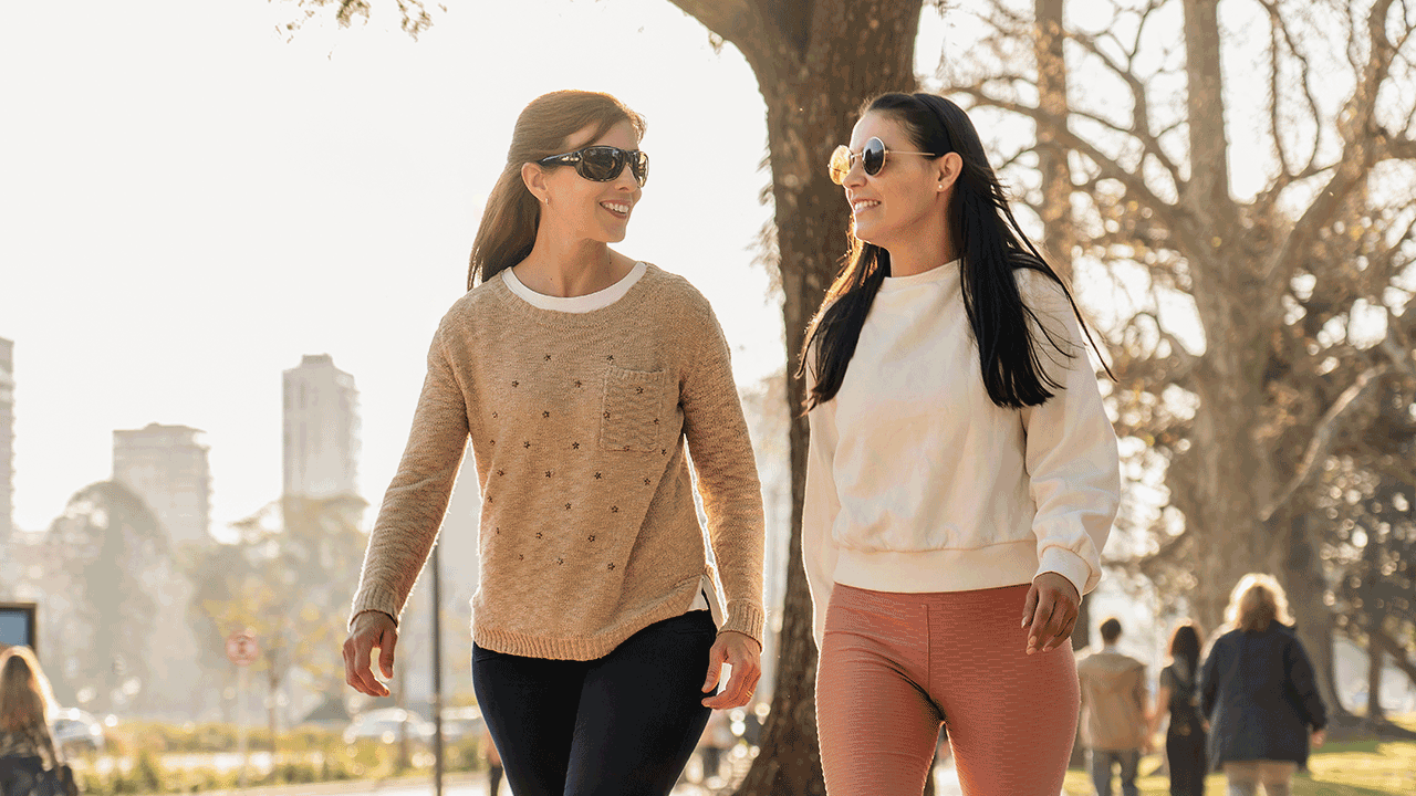 Two women walking and talking in a city park on a sunny day