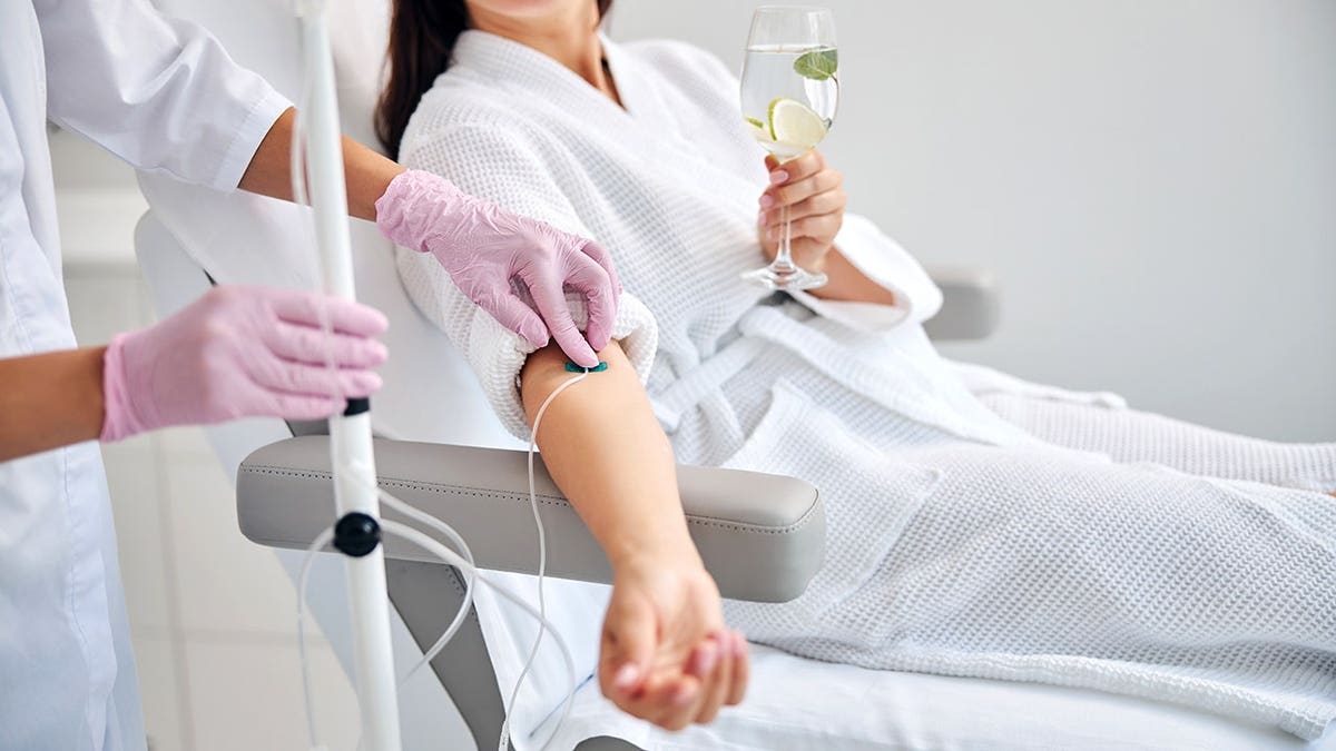 A woman sitting in a cosmetic chair holding a glass of drink.