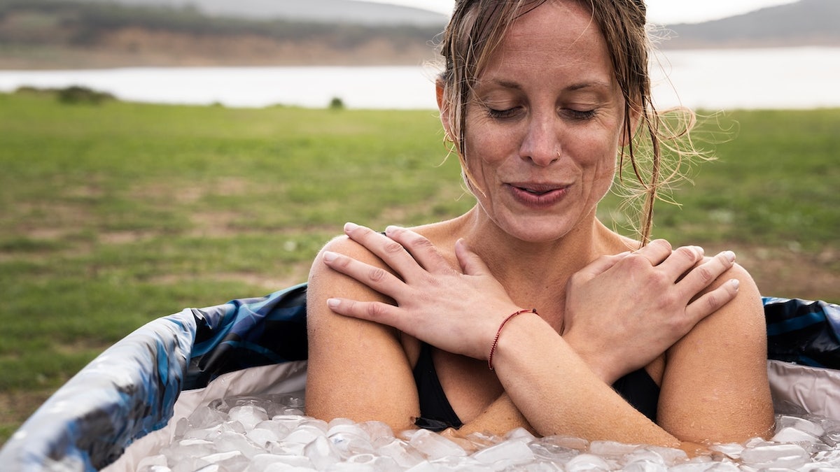 Woman inhaling with eyes closed inside an ice bath tube in a field