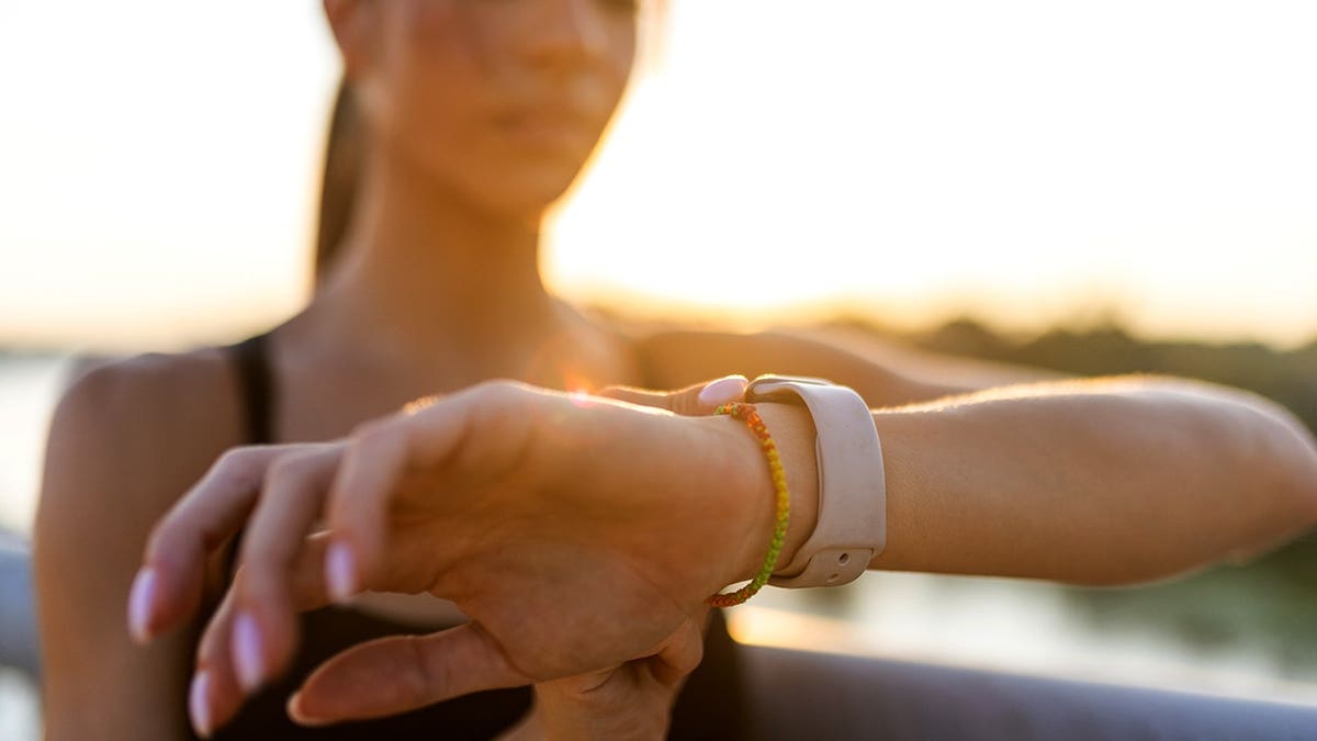 Young woman looking at wristwatch on bridge at sunset before jogging