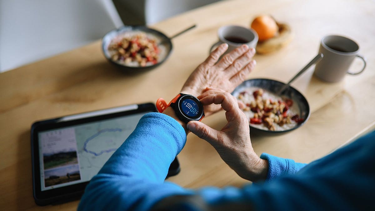 Woman in her 50s setting up a smartwatch outdoors while having a light breakfast