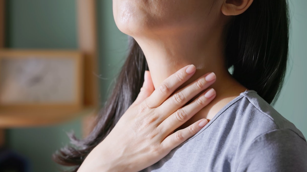 Asian woman holding her neck in pain, showing signs of thyroid gland problem