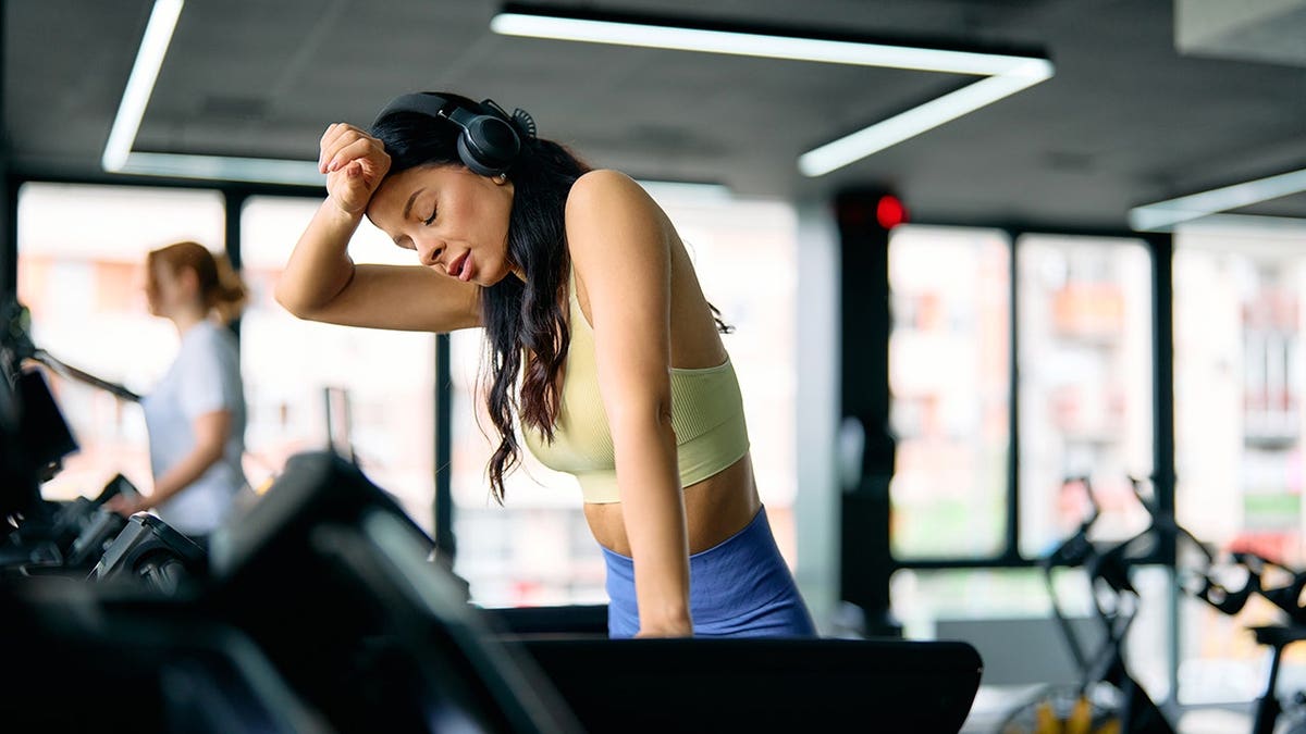 Young athletic woman wiping sweat from her brow during treadmill workout in gym