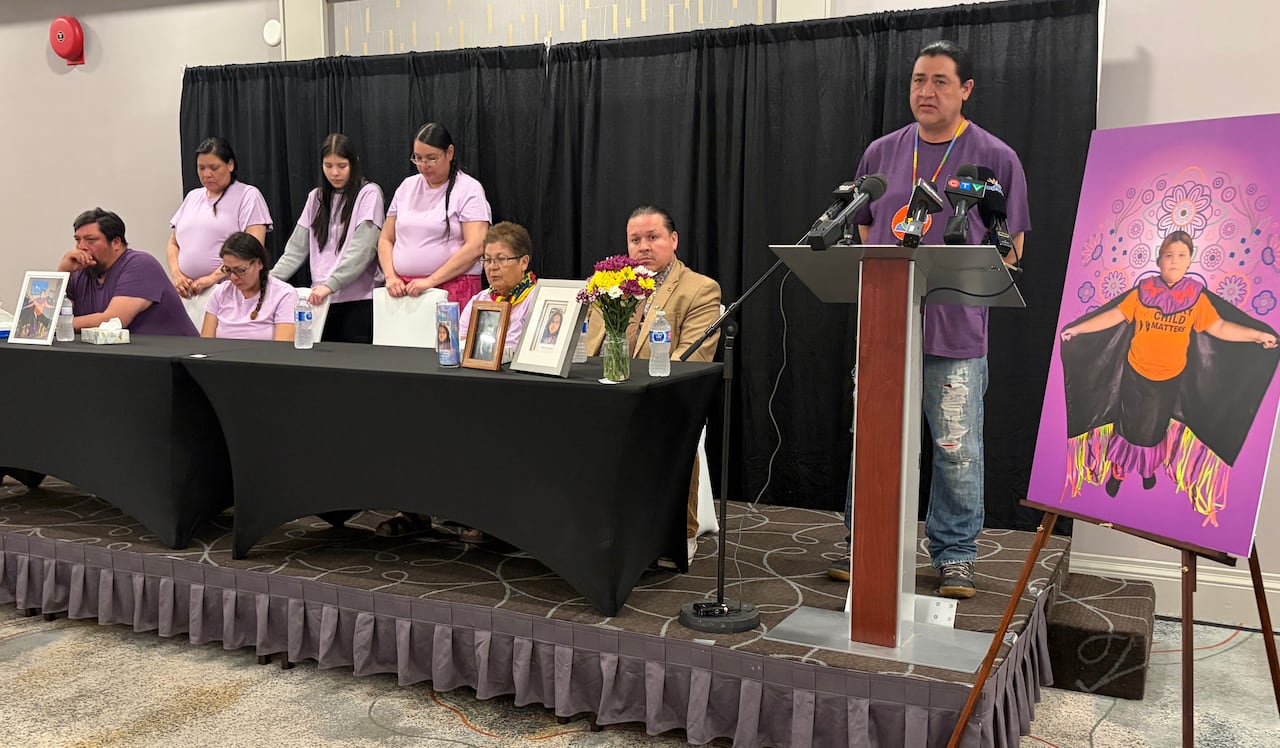 A man speaks at a podium, with a group of people sitting at a table next to him.