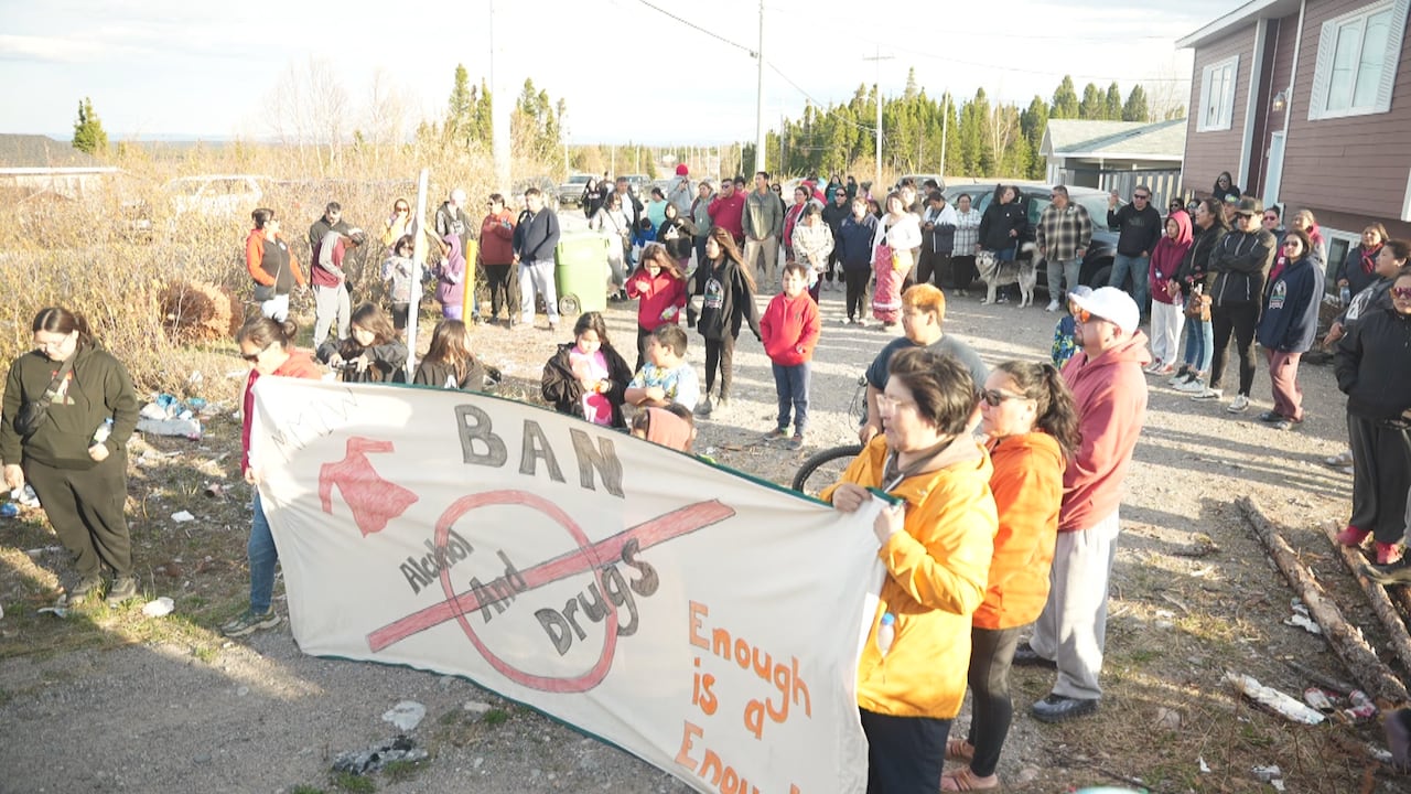 People walked through Sheshatshiu on Thursday. Two people hold a large banner that says 'Ban alcohol and drugs. Enough is enough.'