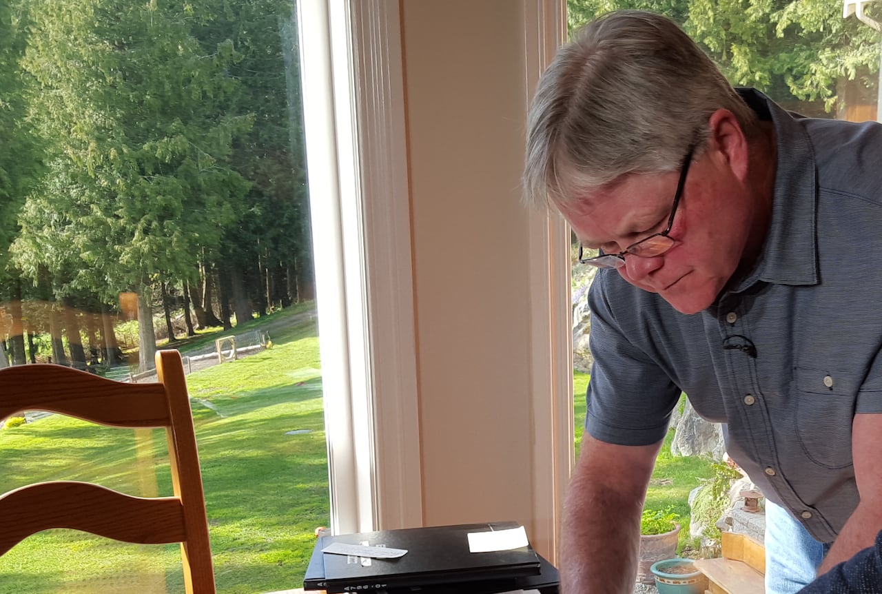 A man with grey hair wearing a blue polo shirt leans over a kitchen table.