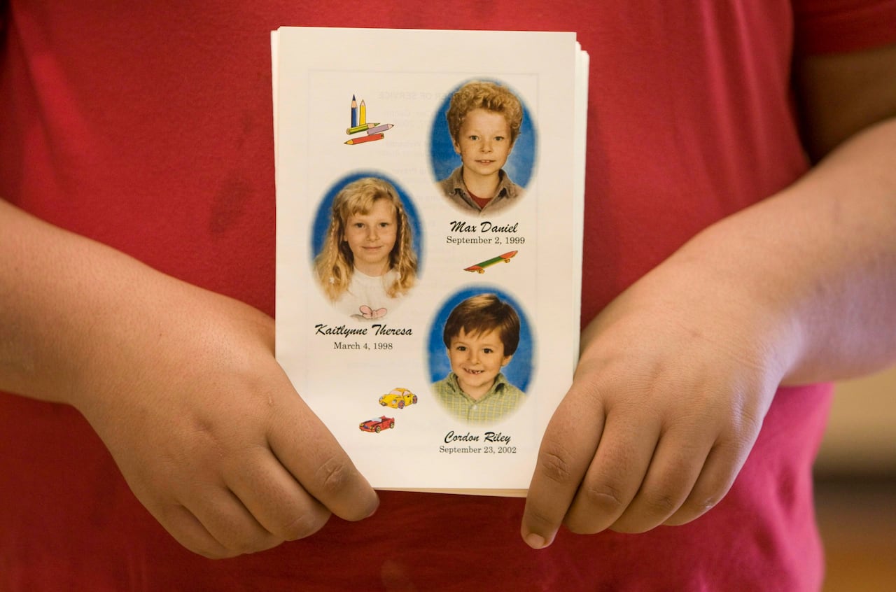 A person holds a card with the pictures of three young children on it.