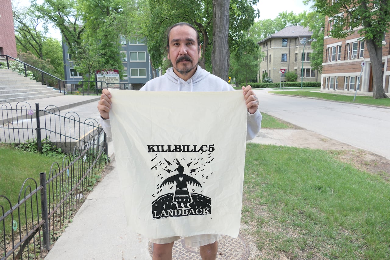 A man holds a sign saying "Kill Bill C5" and "Land Back."