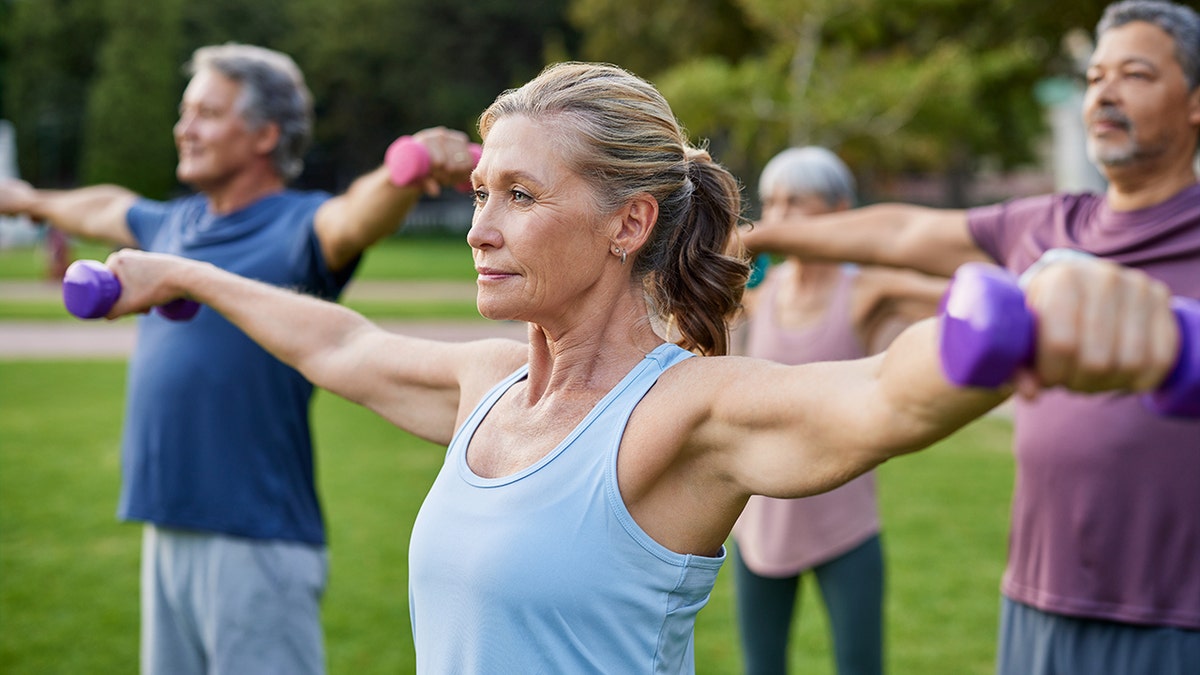 Senior woman lifting dumbbells during outdoor group exercise in park