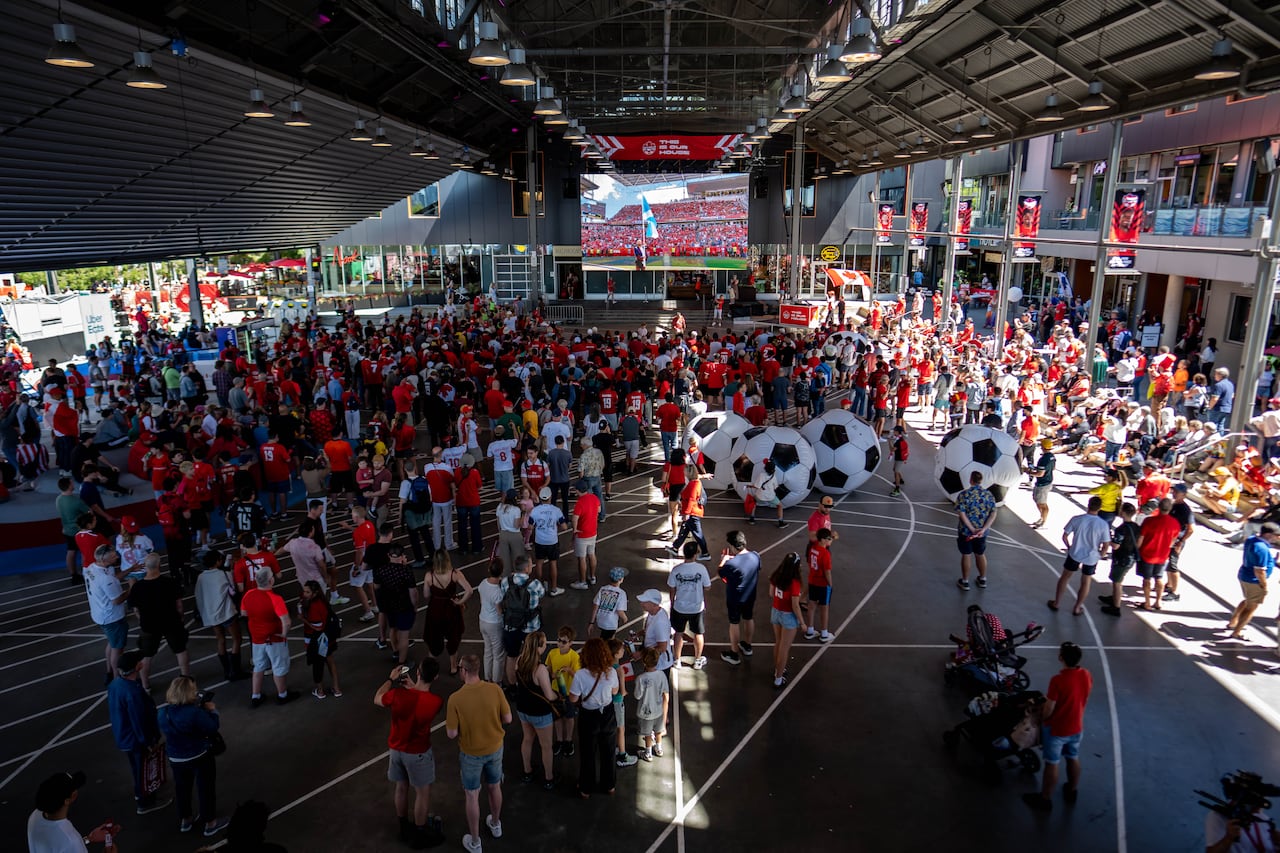 Fans pack into an undercover area with a large screen showing a soccer game.