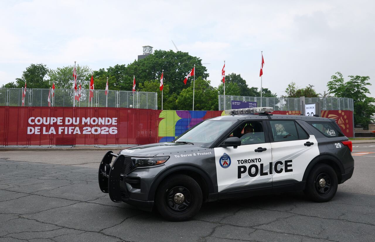 A police vehicle seen parked in a parking lot in front of a fence covered in FIFA World Cup banners and Canadian flags.