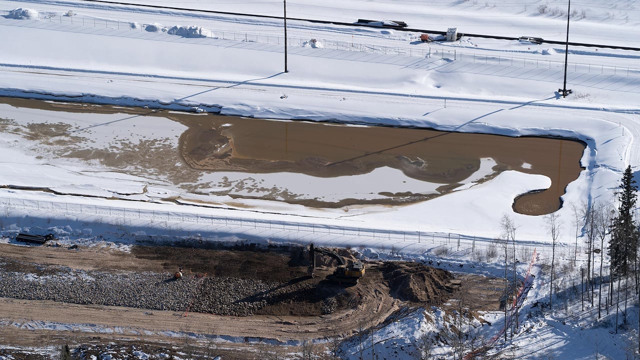 A piece of heavy machinery works on a dirt site next to a wastewater pond.