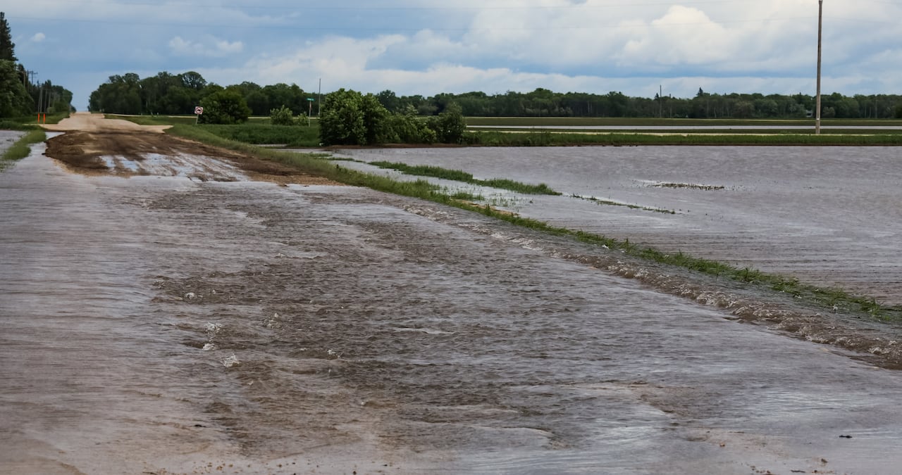 A country road is shown covered in water with a flooded field next to it
