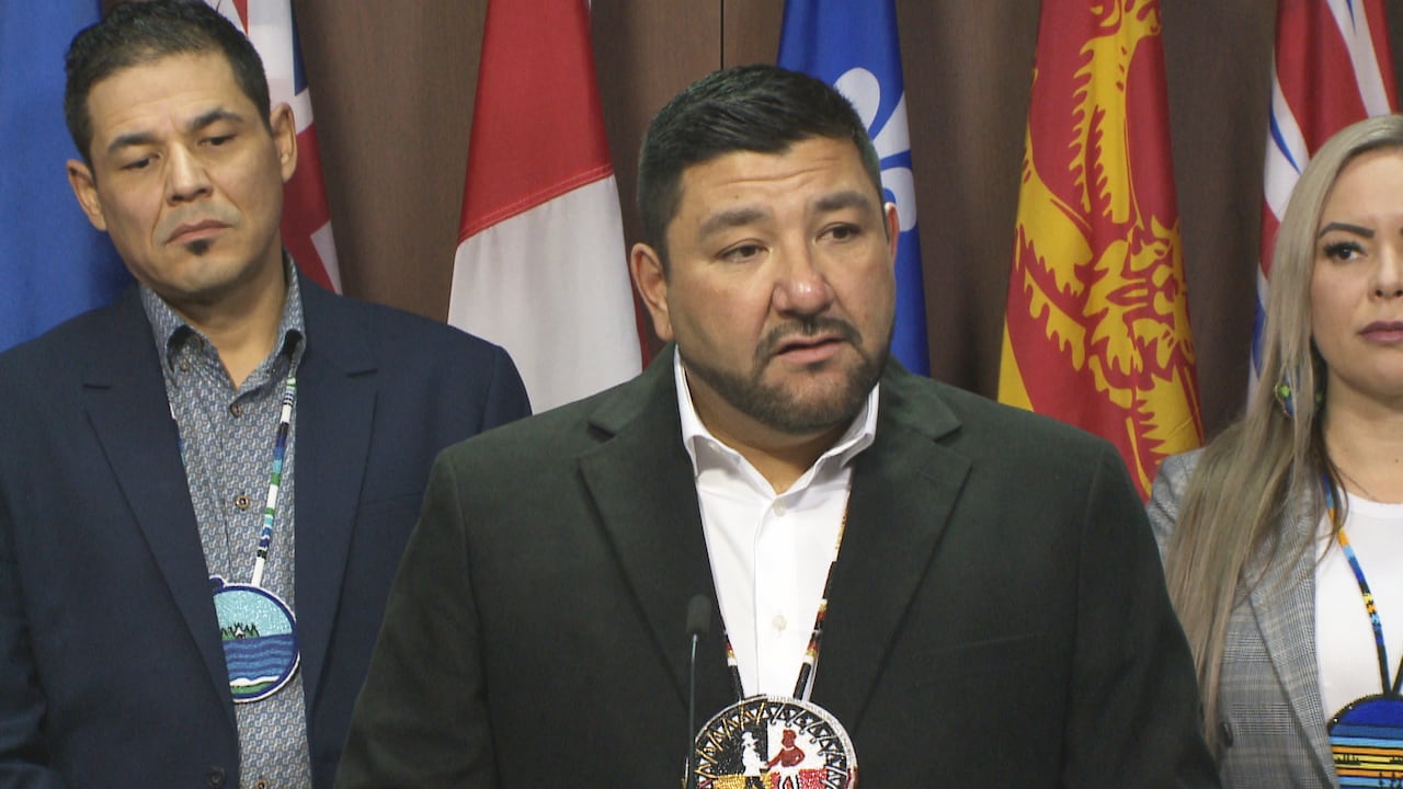 A man stands at a podium with a man to his left and woman to his right