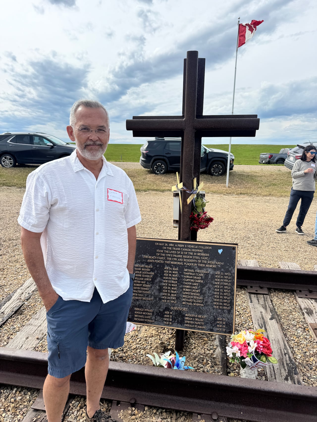 Man in white shirt and shorts stands near an iron cross