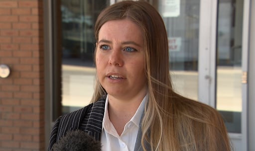 A woman speaks in an interview outside a brick building.