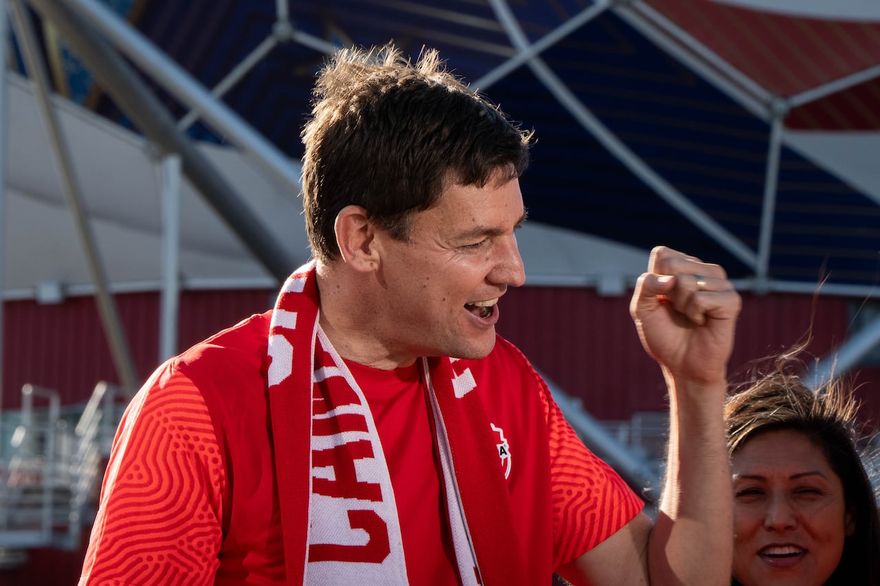 David Eby wears a Canada scarf and jersey and raises a fist in celebration