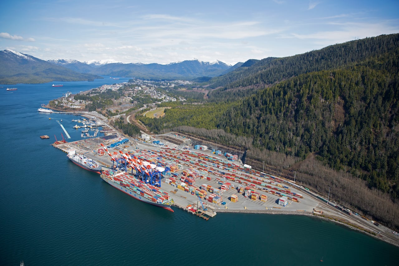 An industrial port seen from the air hugs a green mountainside.
