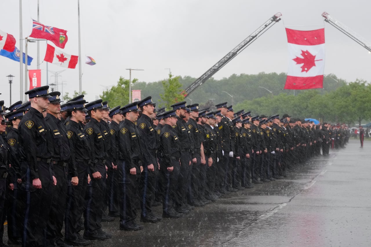 Officers stand by a road with a Canadian flag flying above.