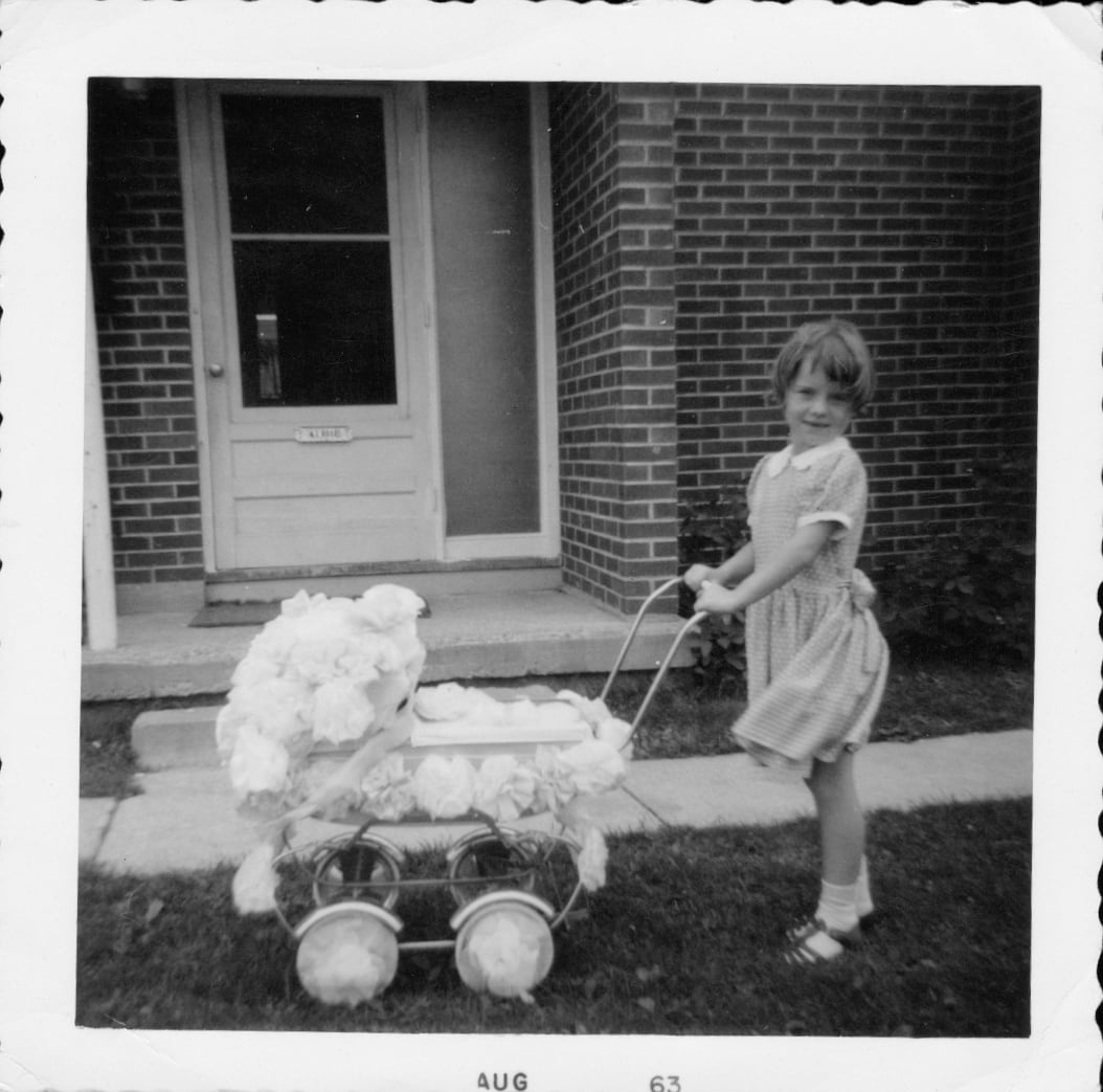 A black and white photo of a little girl with a doll's carriage.
