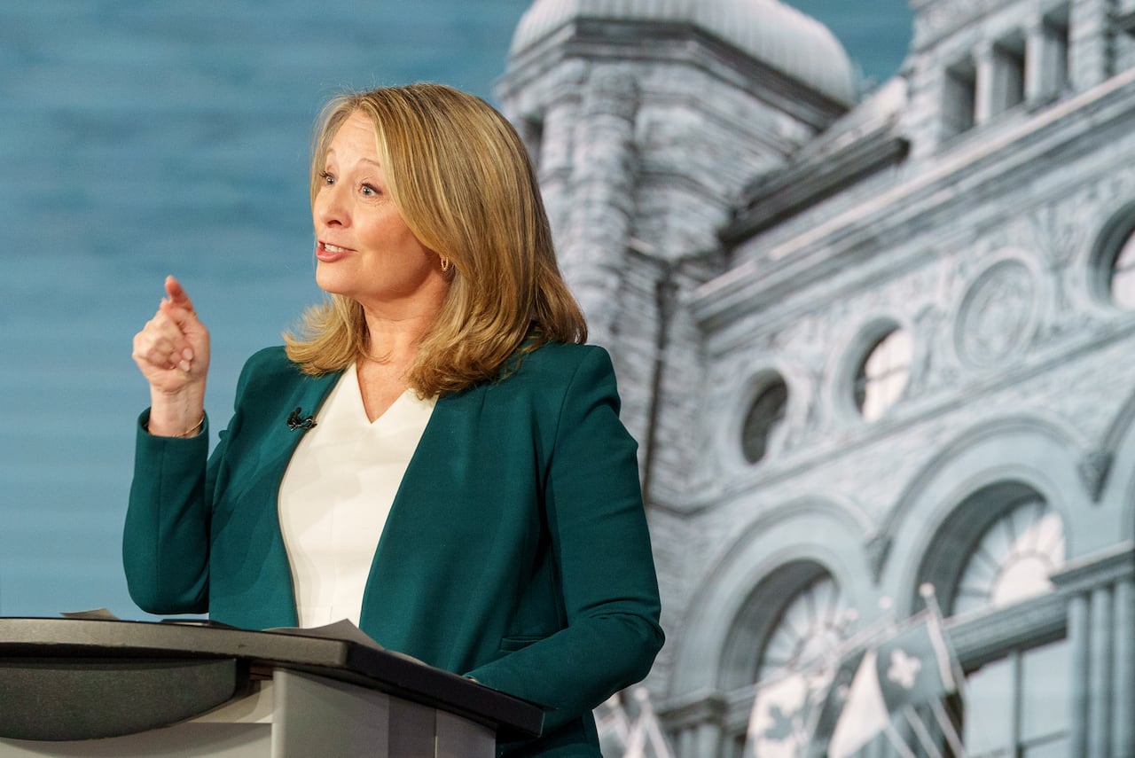 A woman in a green jacket speaks from a podium.