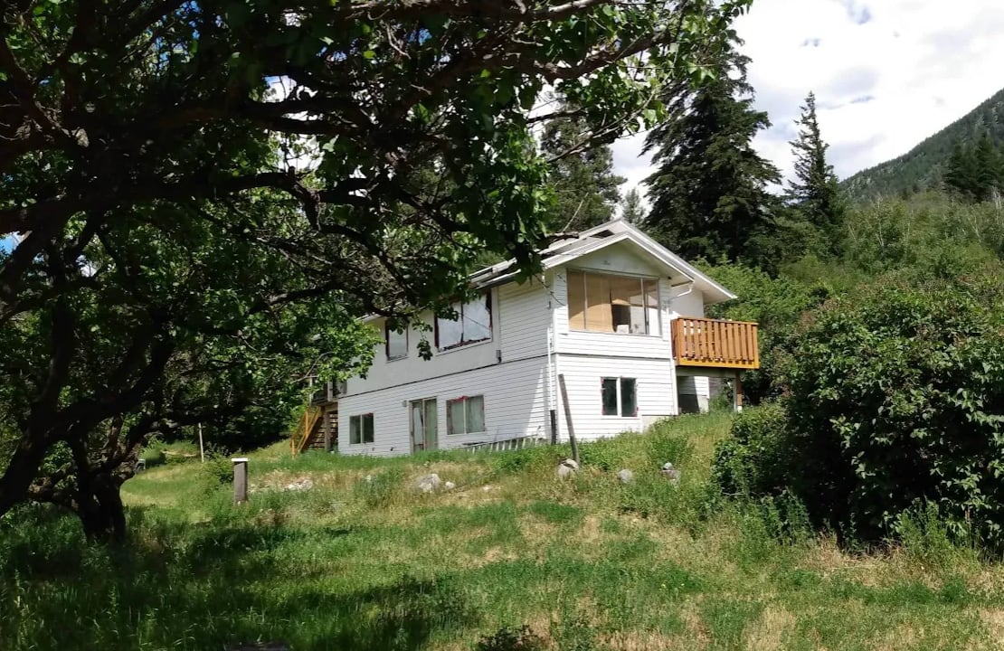 A white house among grass, trees and bushes.