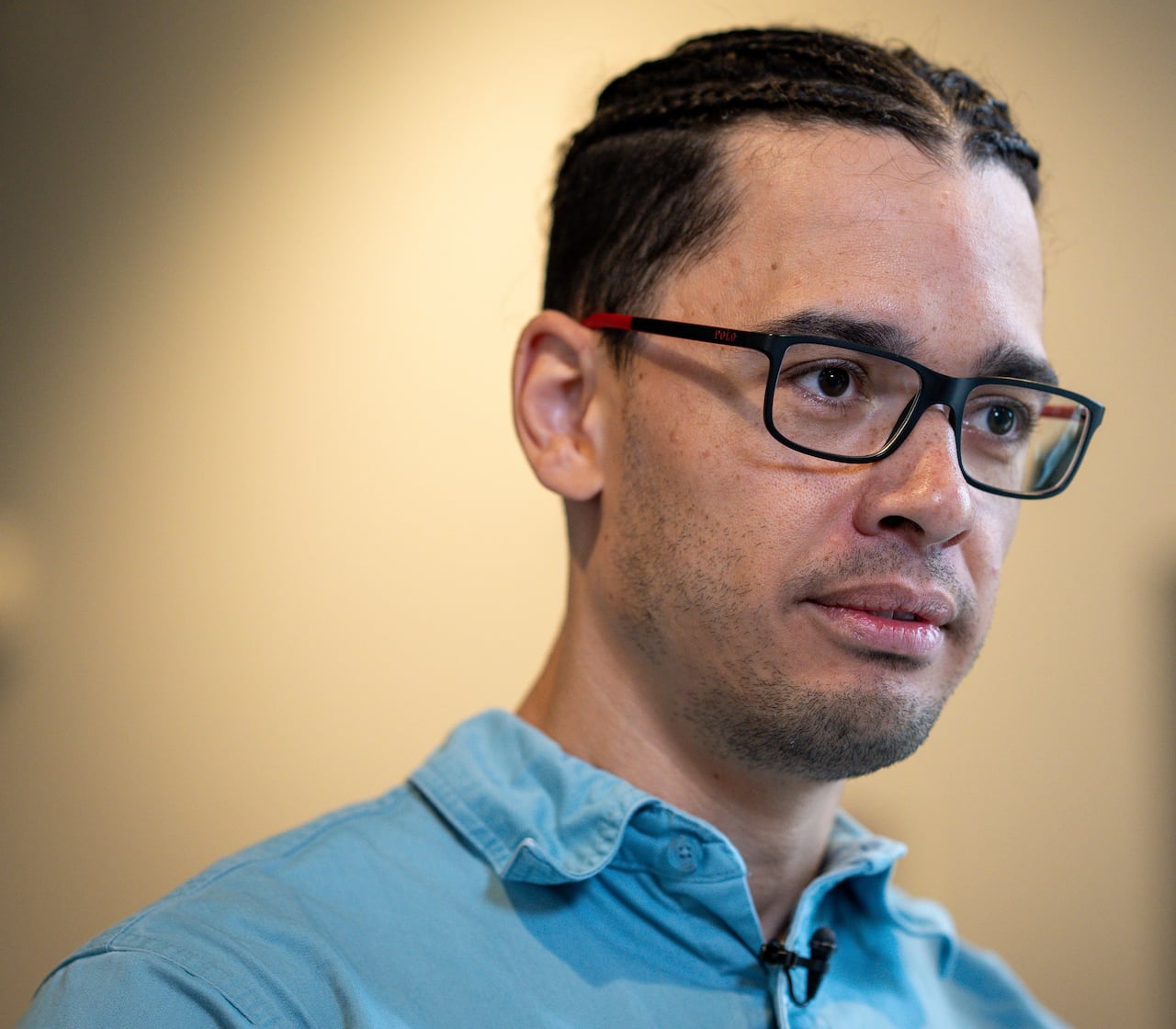 A man wearing a blue shirt and glasses looks on.