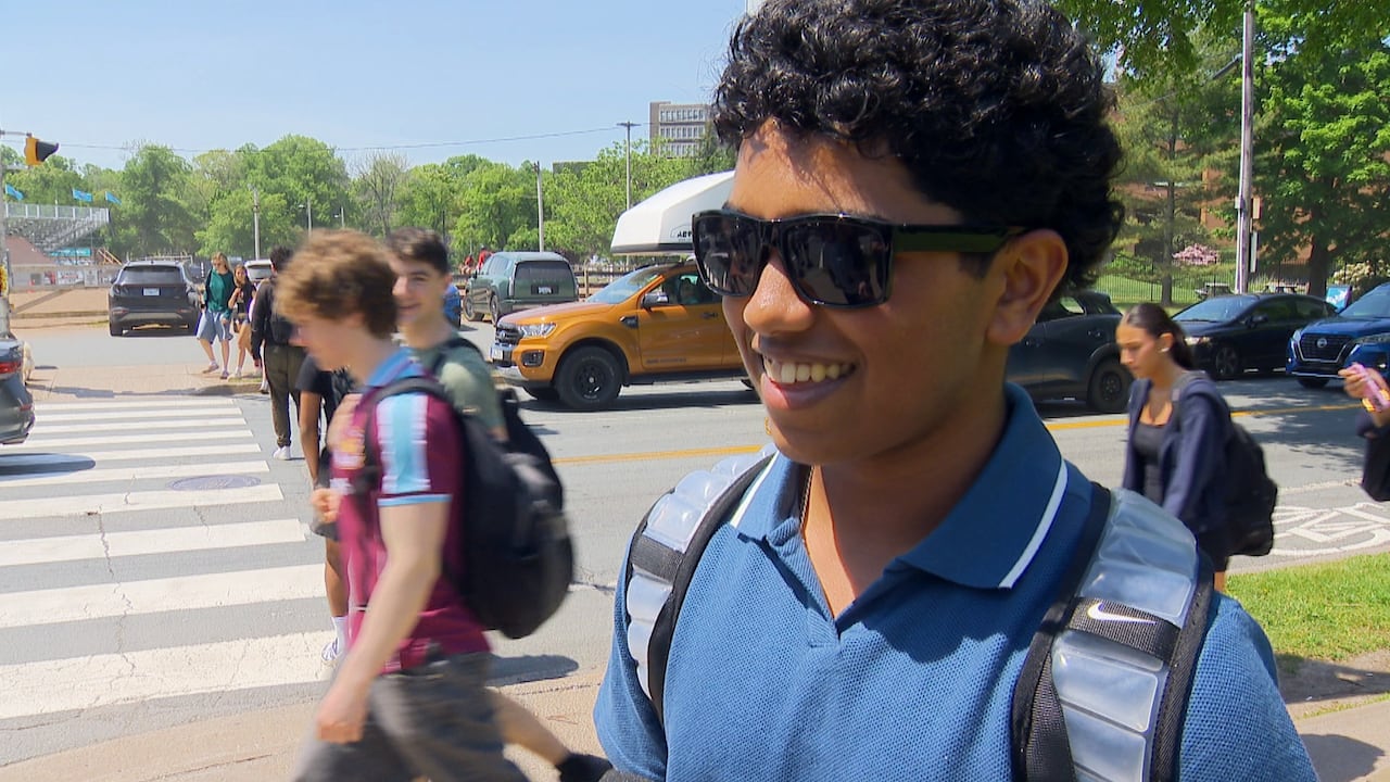 A boy wears black sunglasses and a blue polo shirt. Her has dark brown curly hair.