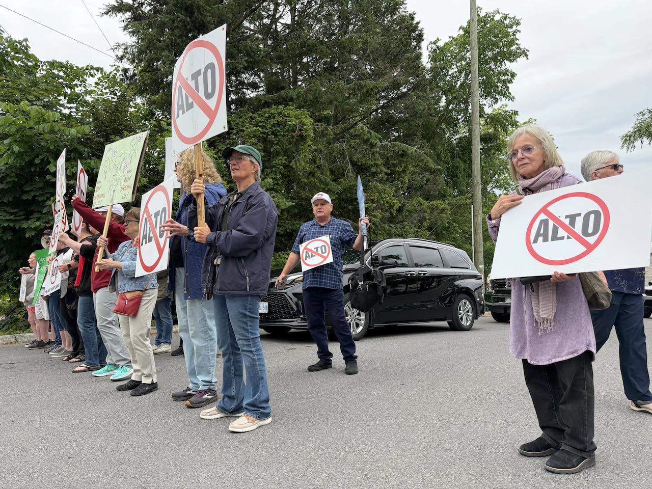 Protesters stand in the street holding anti ALTO signs.