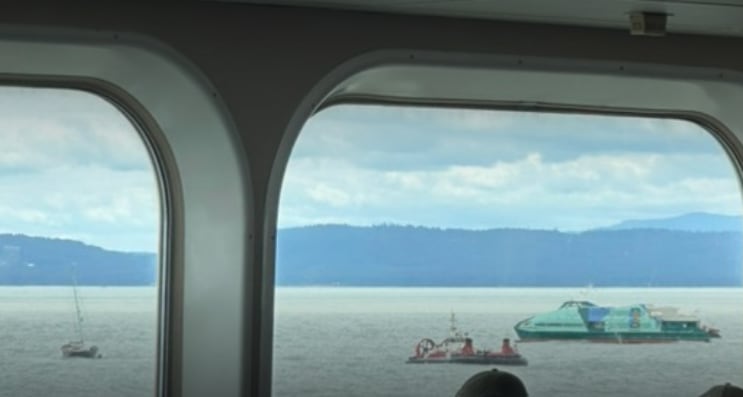 A Canadian Coast Guard hovercraft and a Hullo passenger ferry seen near a sailboat through the window of a B.C. ferry.