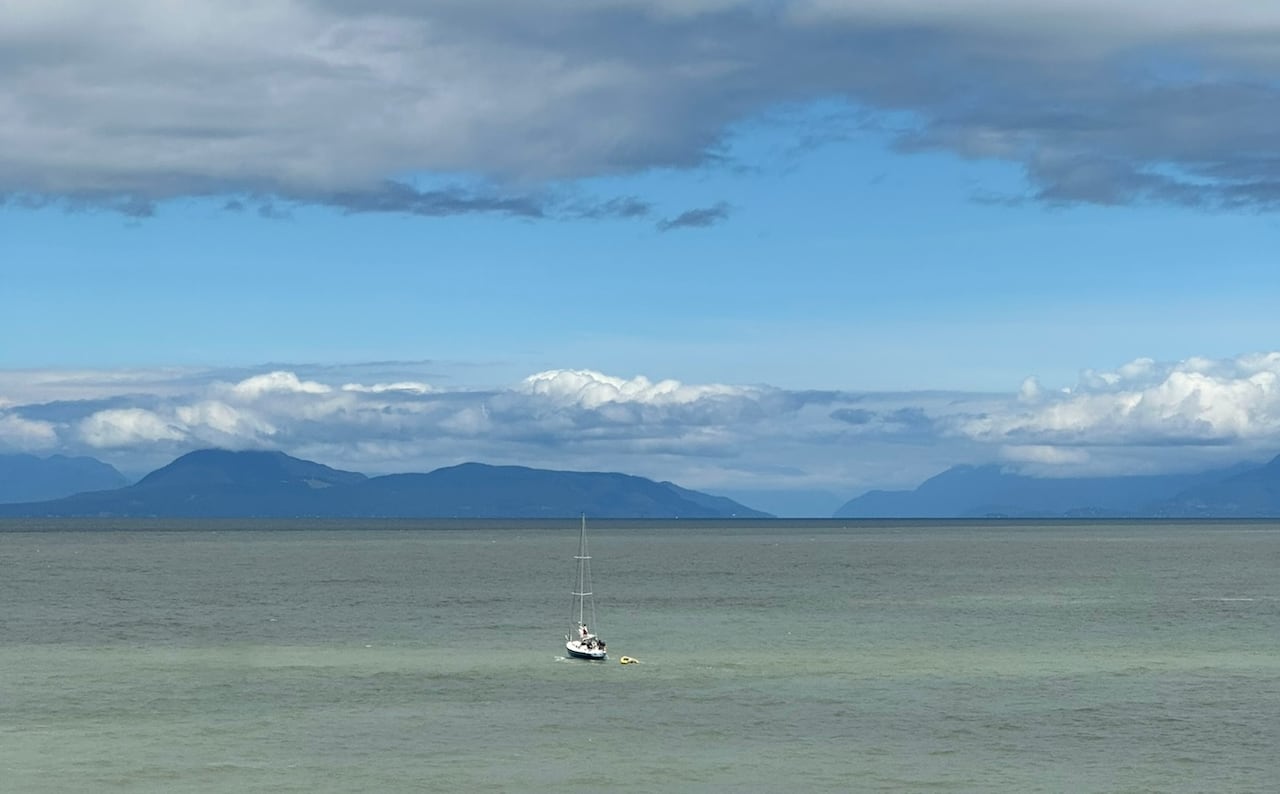 A sailboat towing a dinghy with the mountains in the background.