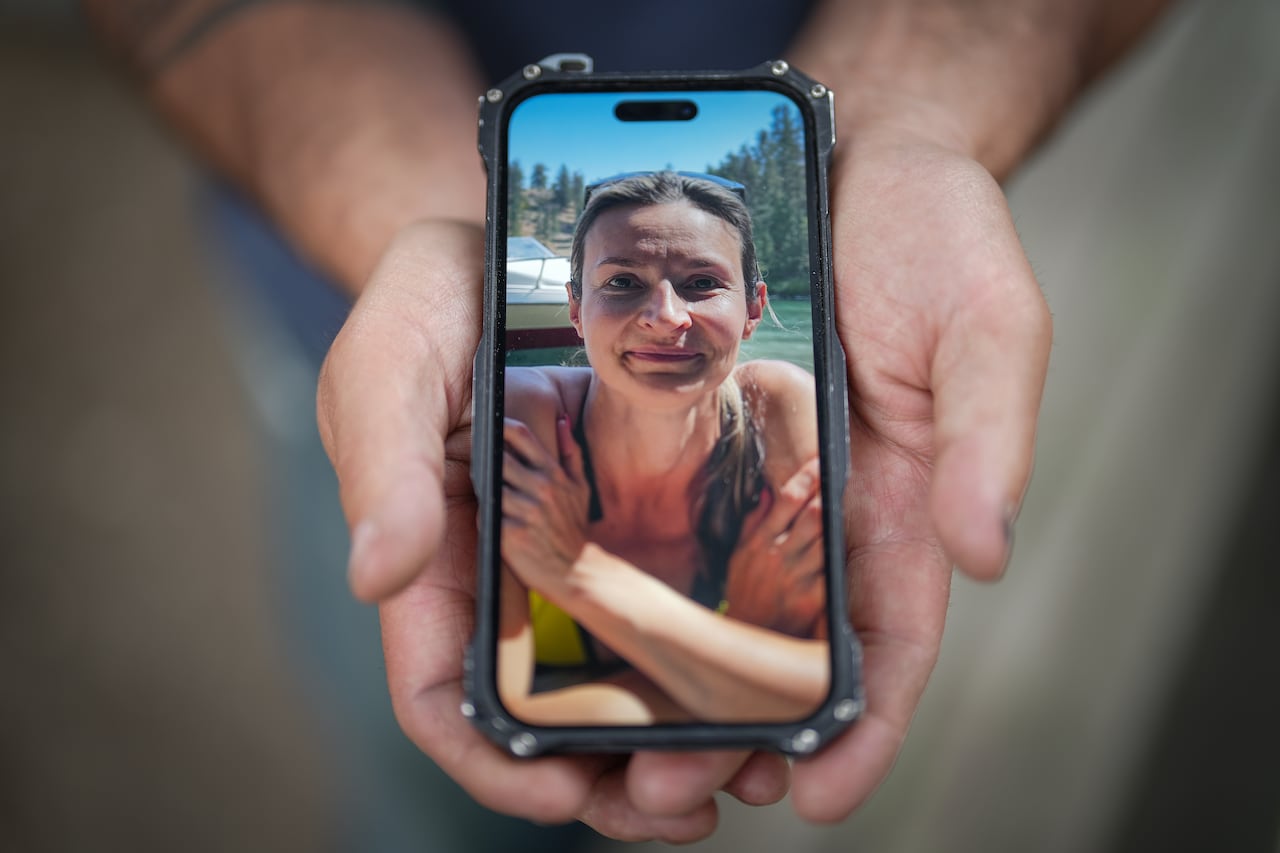 A person holds a smartphone displaying a close-up photo of a woman outdoors.