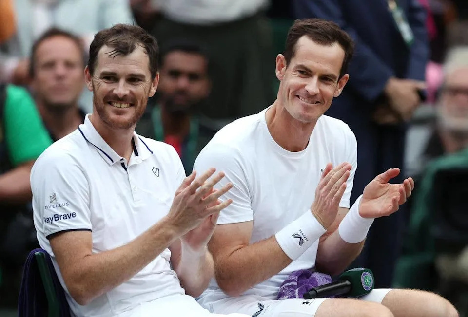 Andy Murray and Jamie Murray applaud while sat on the side of the court at Wimbledon in 2024.