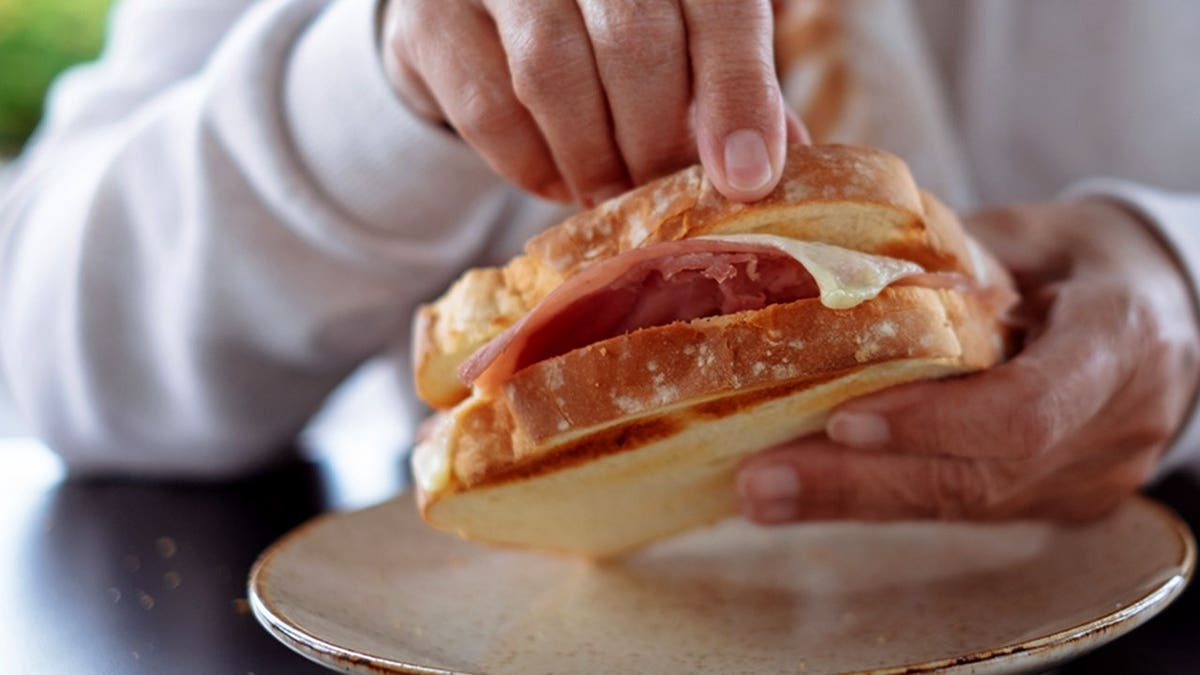 Elderly woman holding french toast while sitting at an outdoor cafe table