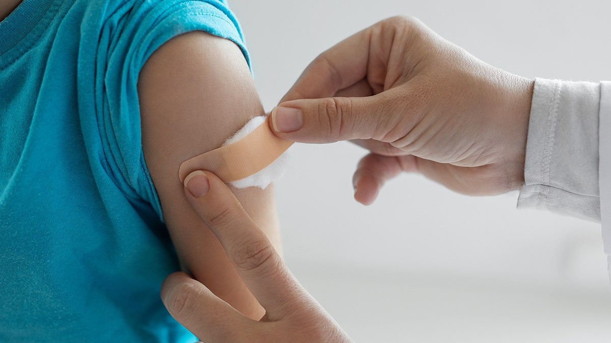 Doctor applying band aid on patient's shoulder after flu shot vaccination