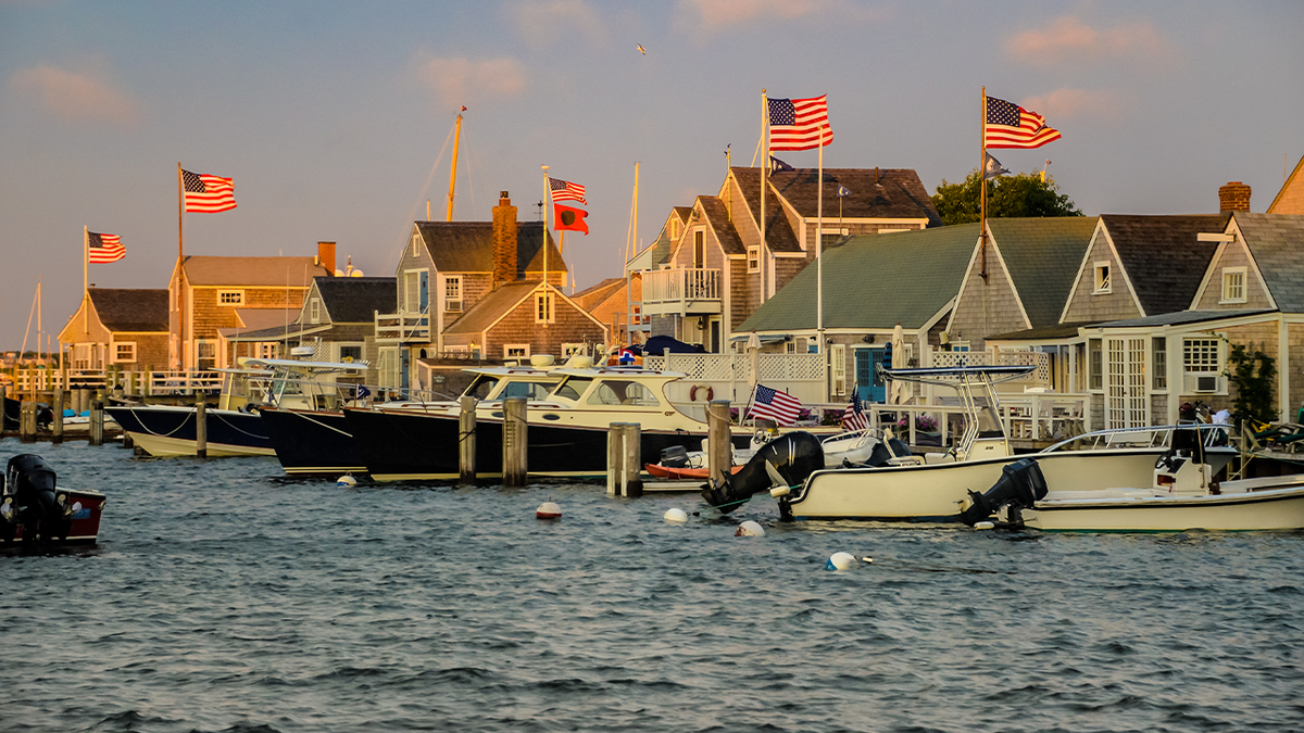 Boats docked in a marina in Nantucket in front of waterfront houses flying American flags