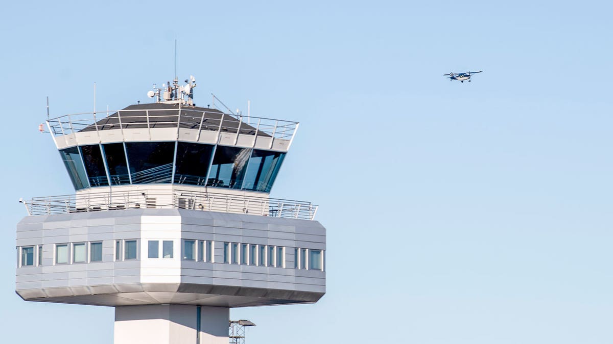 Air traffic control tower at Flesland Airport with a small propeller plane flying in the background