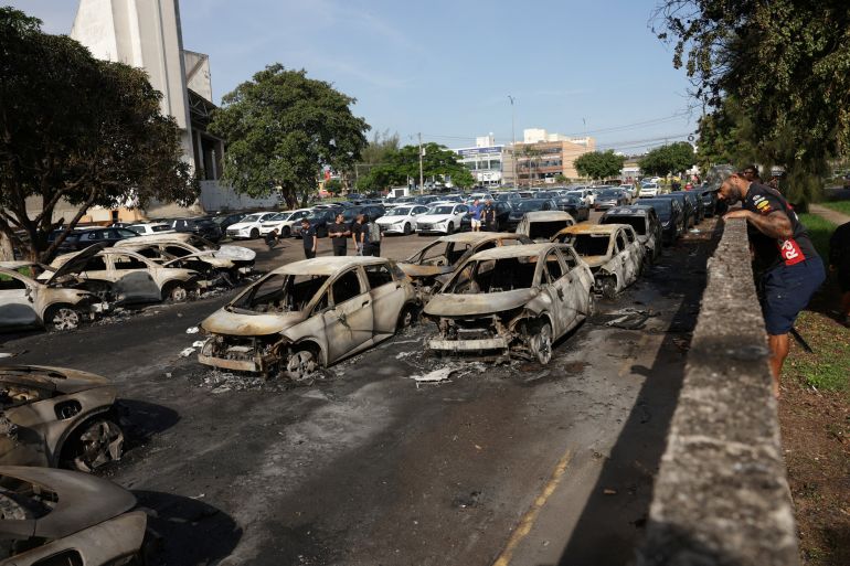 People gather near charred vehicles following a deadly collision between two helicopters in Rio de Janeiro, Brazil, June 14, 2026. REUTERS/Ricardo Moraes