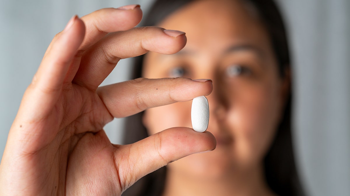 woman holds a white pill in between her fingers