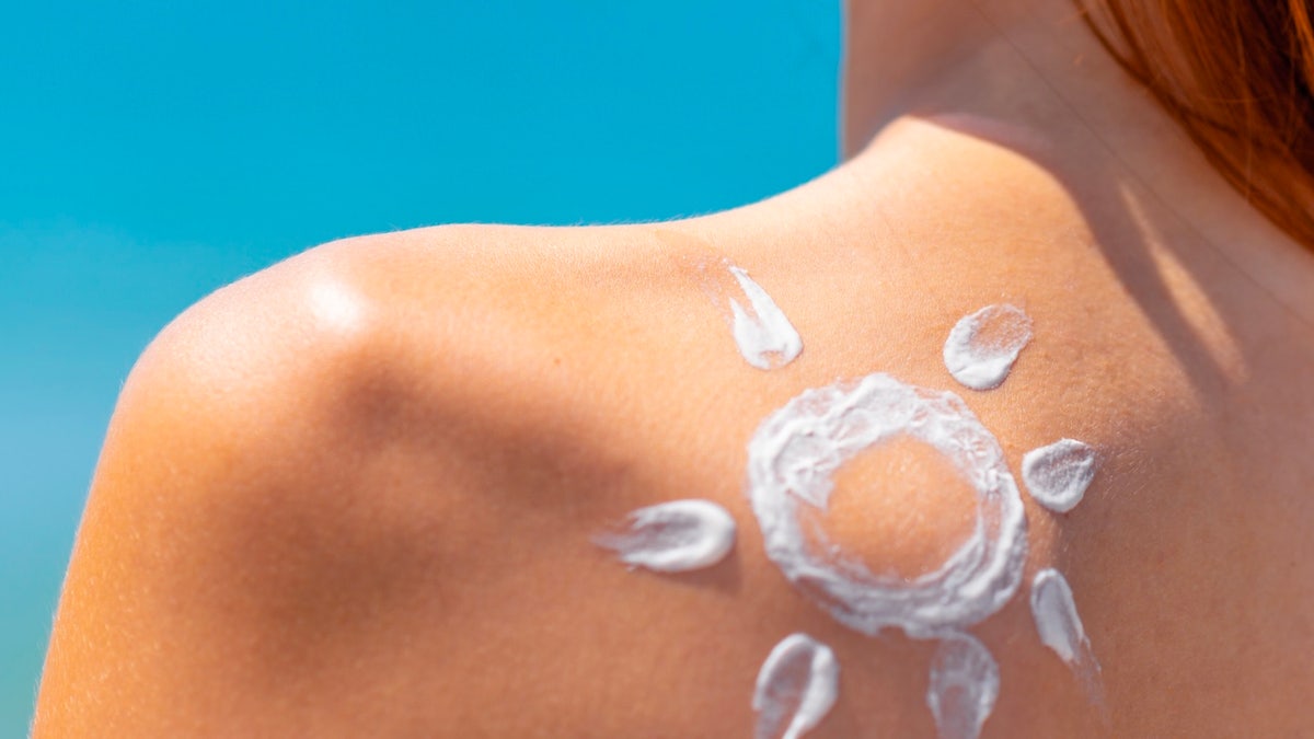 Tan woman applying sunscreen lotion on her shoulder at the beach