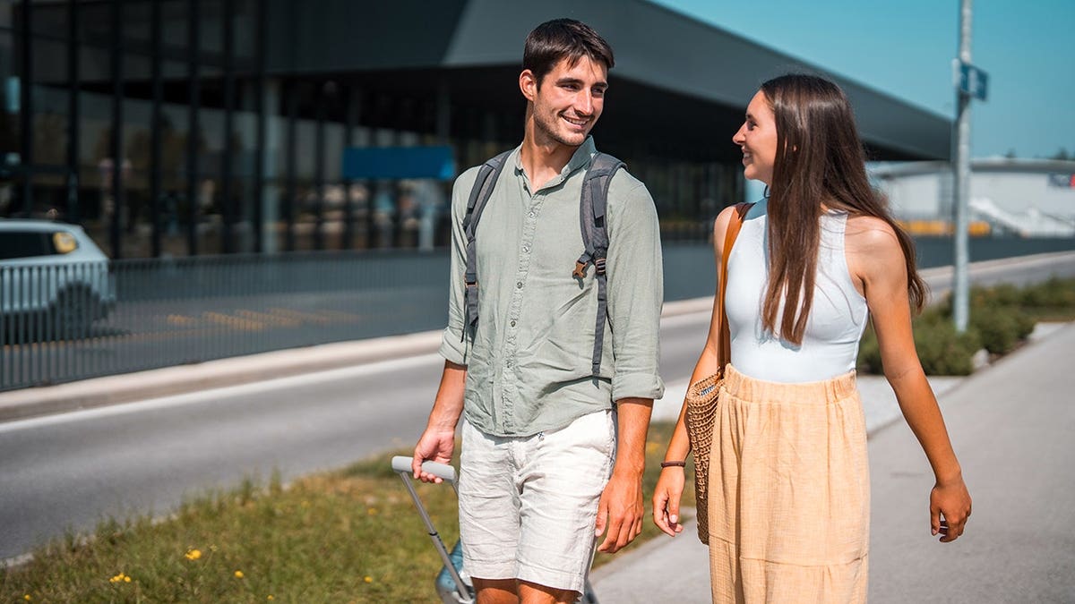 Young Caucasian couple strolling outside airport terminal exchanging happy glances