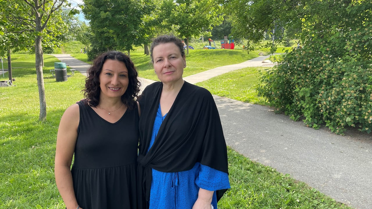 Two women stand in a park.