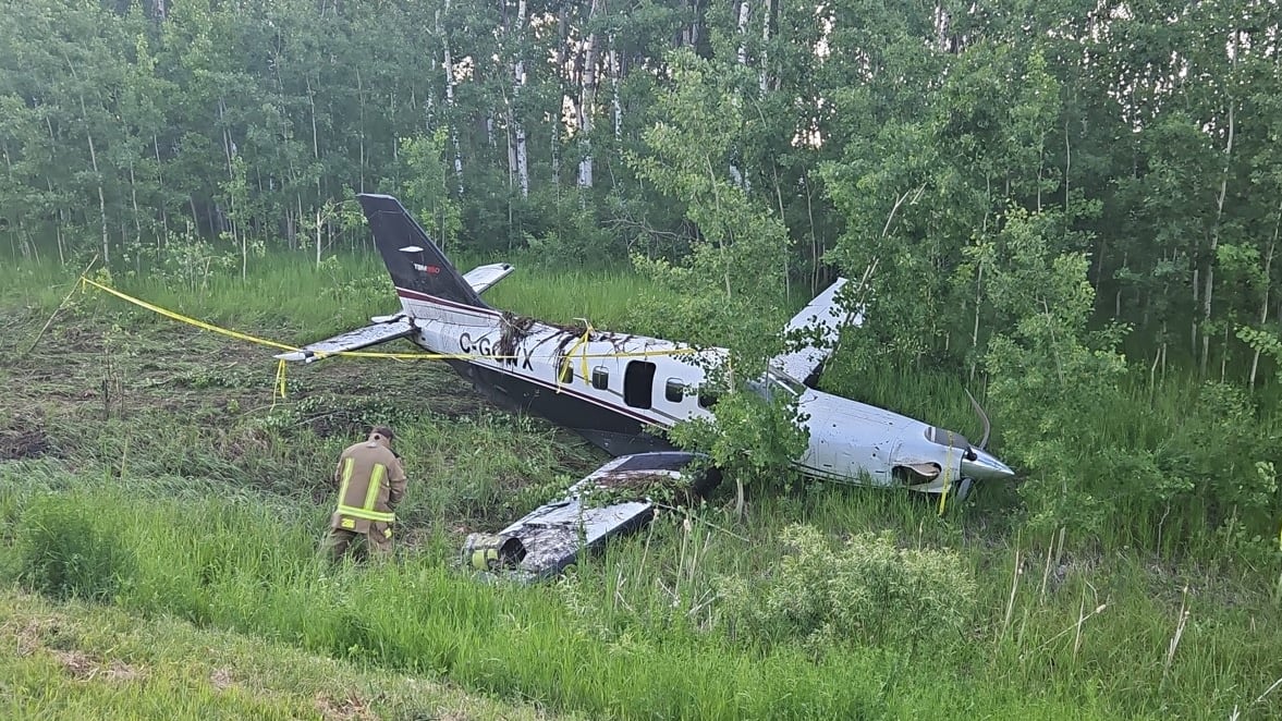 A small-engine plane sits in a grassy ditch after making an emergency landing on a rural highway.