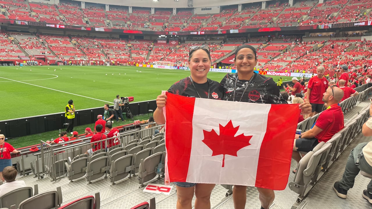 Two women hold a Canadian flag at in the stands of a FIFA World Cup match.